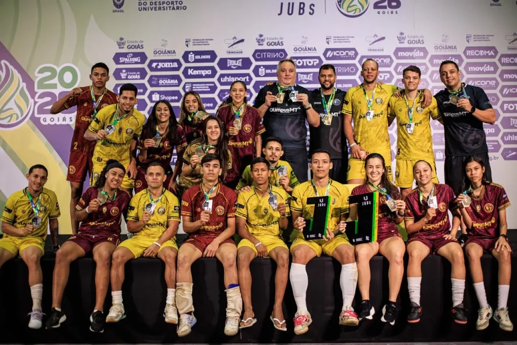 Atletas do futsal feminino da FAIPE MT no pódio recebendo as medalhas de ouro e a taça de campeãs dos JUBs Goiás 2026